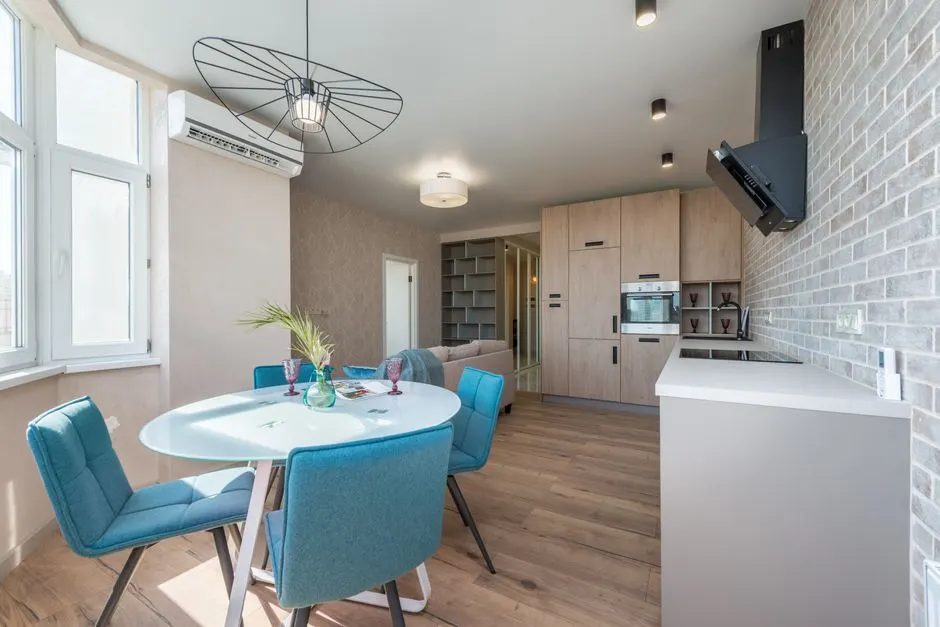 Modern interior design of new spacious studio with beige kitchen furniture near round dining table and big sofa in daytime