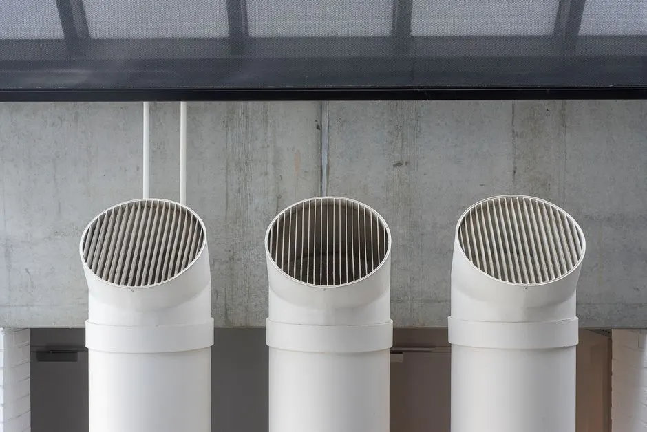 Three white industrial ventilation pipes aligned on concrete wall.